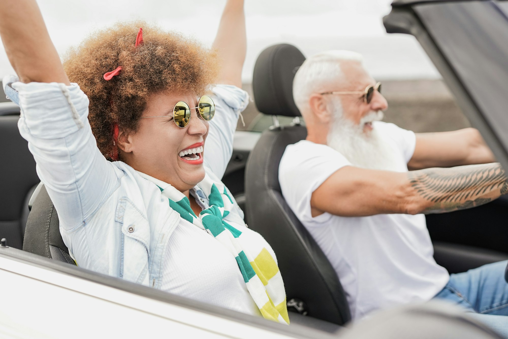 Senior multiracial couple having fun with convertible car during road trip vacation